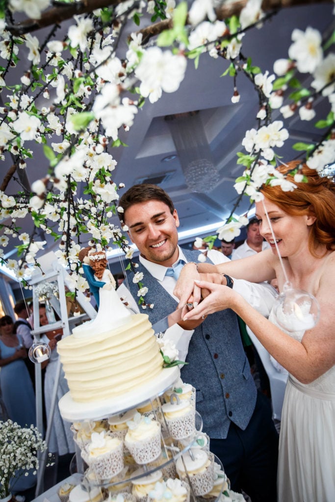 Bride and groom cutting the cupcake tower top cake surrounded by apple blossom