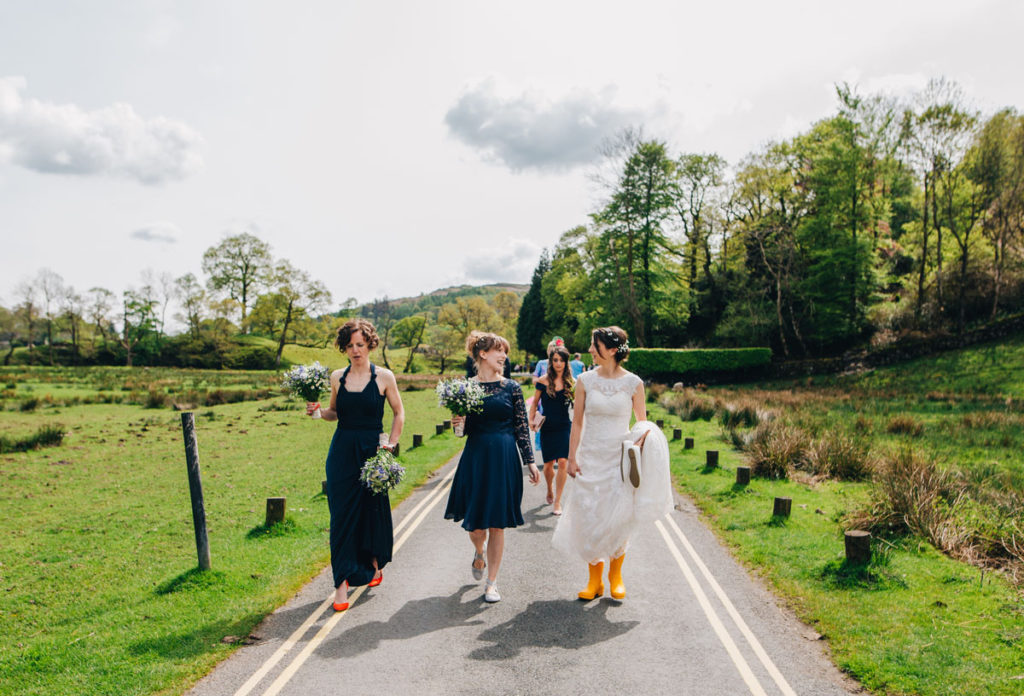 Bride and bridesmaids walking to the wedding venue. Bride in yellow wellington boots